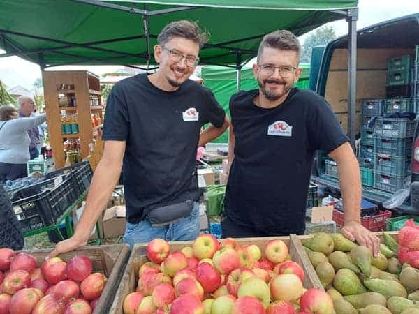 Szymon i Jakub Celmer przy stoisku z jabłkami i gruszkami na targu